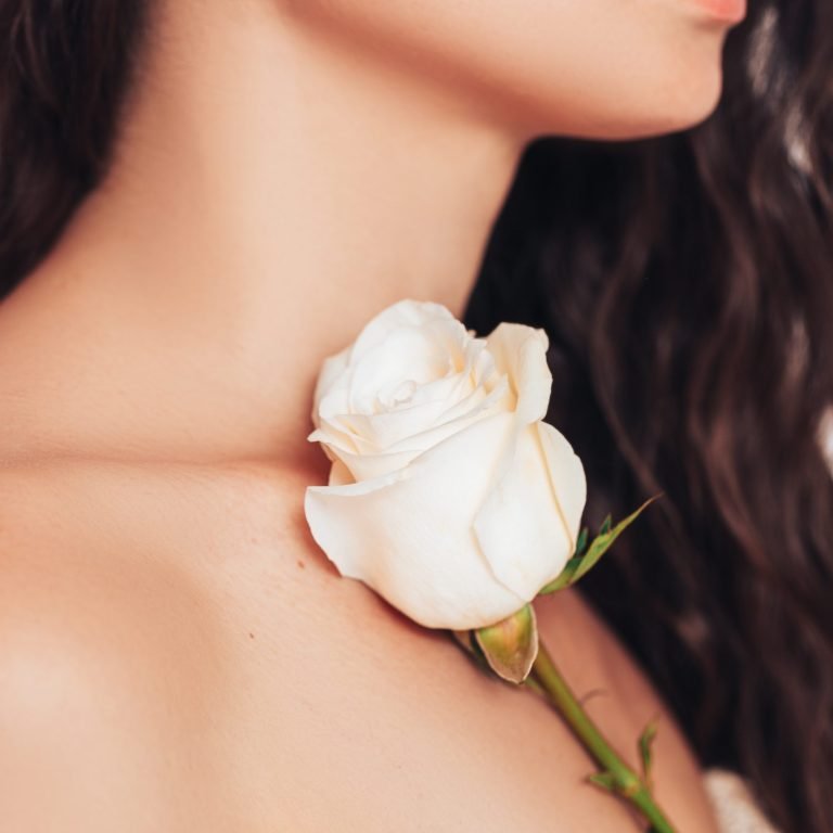 Young woman on a white background with loose hair put a pink rose on her shoulder.